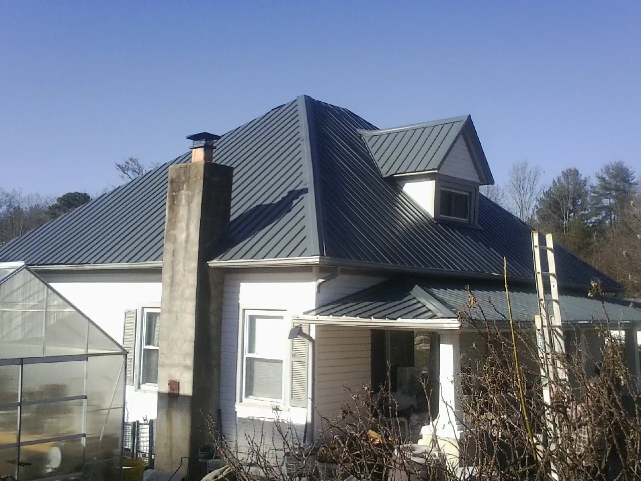 Dark blue standing seam metal roof on a white farmhouse with dormer — Slate & Tile Roof Repair by Roofing Brothers in Belden