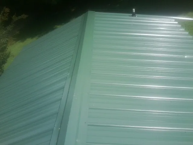 New green metal panels meeting at the ridge of a roof — Flat Roof Repair work by our crew in Belden